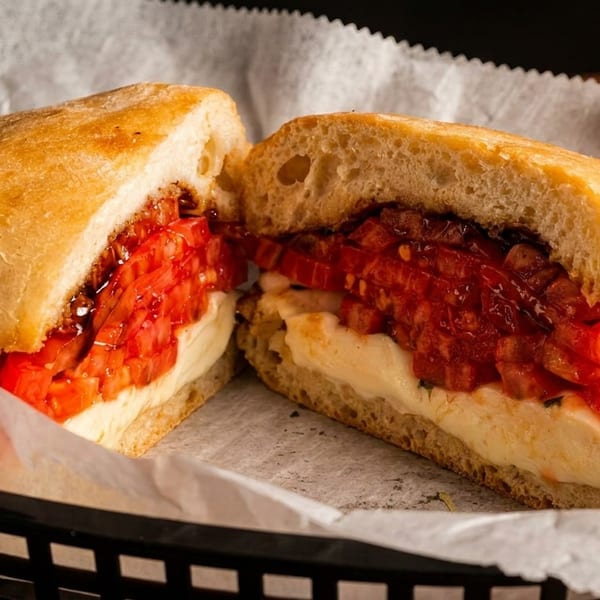 A sliced caprese sandwich with fresh mozzarella, red tomatoes, and balsamic glaze on ciabatta bread.