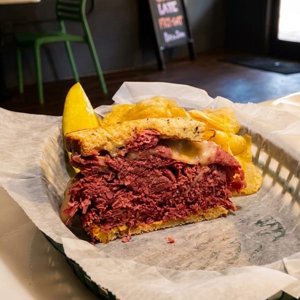 A large pastrami sandwich with melted cheese, chips, and a pickle spear in a basket.
