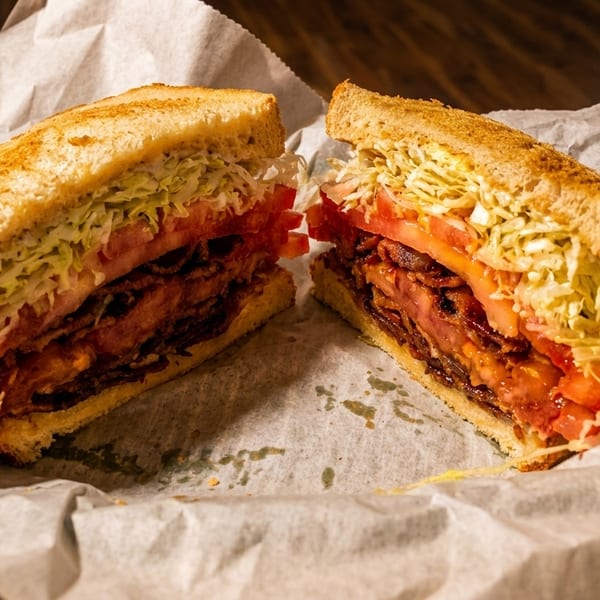 A large BLT sandwich, cut in half, with crispy bacon, fresh tomatoes, and shredded lettuce.