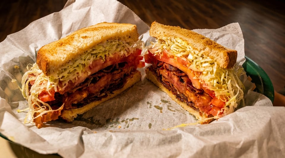 A large BLT sandwich, cut in half, with crispy bacon, fresh tomatoes, and shredded lettuce.