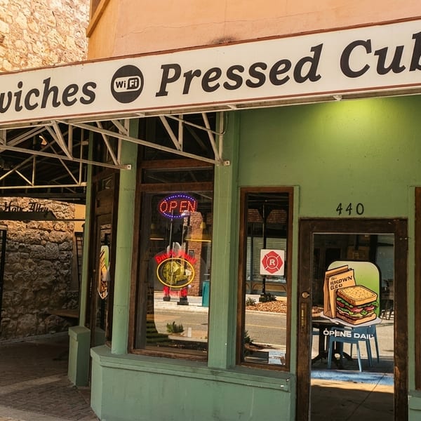 Exterior of a green building with a "Sandwiches Pressed Cubans" sign and an "Open" neon sign.